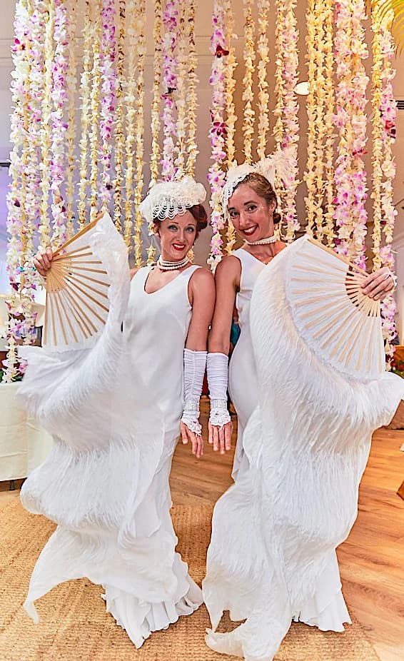 Two white fan greeters posing in front of floral decor